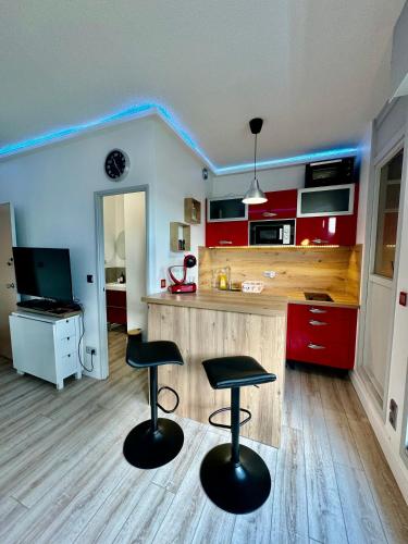 une cuisine avec des placards rouges et deux tabourets de bar dans l'établissement Appartement centre ville - Accès piscine - 300M de la plage, à La Grande Motte