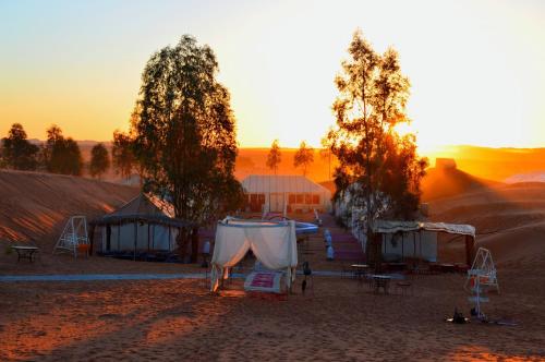 a group of tents in the desert at sunset at Merzouga Paradise Luxury Camp in Merzouga