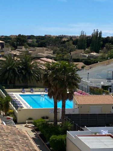 - une vue sur la piscine bordée de palmiers et de bâtiments dans l'établissement Studio Village Naturiste, au Cap d'Agde