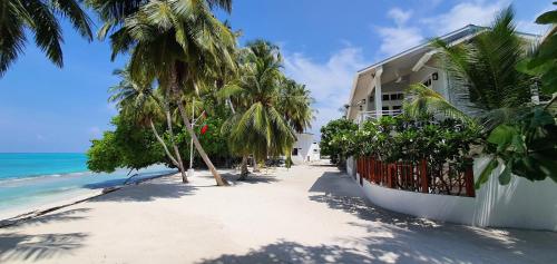 a building on a beach with palm trees and the ocean at The Fulhadhoo Beach Cottage in Fulhadhoo
