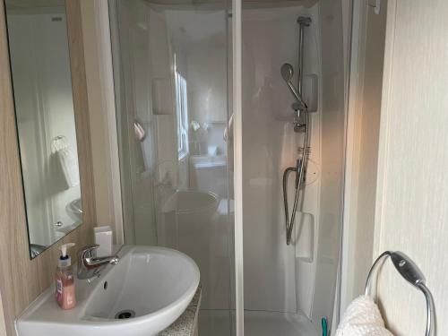 ein weißes Bad mit einer Dusche und einem Waschbecken in der Unterkunft Olivia Ann in Caernarfon