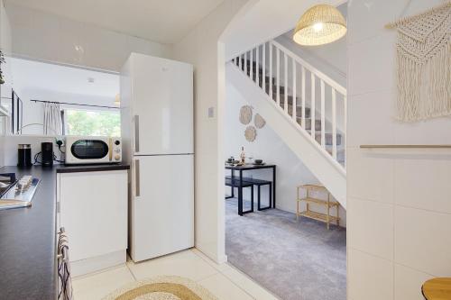 a white kitchen with a refrigerator and a staircase at Seapoint- Boho Coastal Retreat near Sandbanks! in Poole