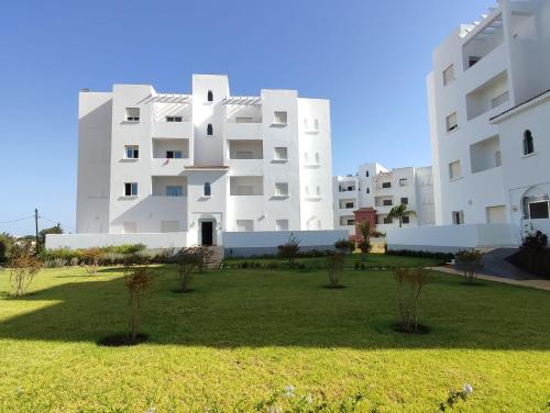 a large white building with a grass field in front at Très bel appartement dans les splendides jardins d'Asilah in Asilah