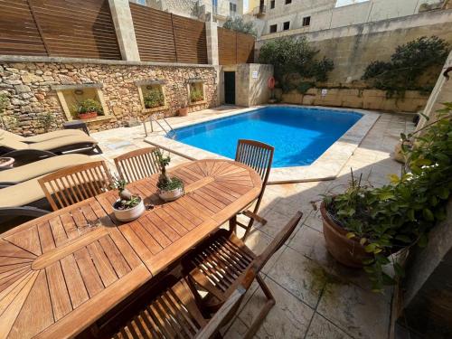 a wooden table and chairs next to a swimming pool at Tal-Mans Farmhouse Gozo in Sannat