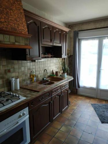 une cuisine avec des armoires en bois, un évier et une fenêtre dans l'établissement Jolie longère au calme proche du Futuroscope, à Saint-Georges-lès-Baillargeaux