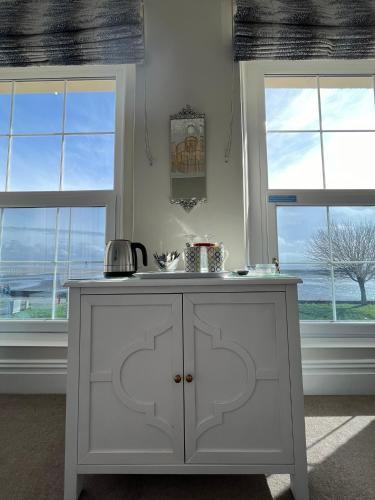 a kitchen with a white cabinet and two windows at Tides Reach Guest House in The Mumbles