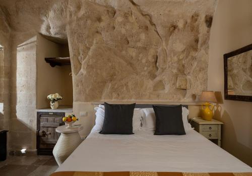 a bedroom with a white bed with a stone wall at Locanda Di San Martino Hotel & Thermae Romanae in Matera