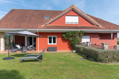 a red house with a bench and an umbrella at Villa entre Santander y Cabárceno con piscina in Revilla de Camargo