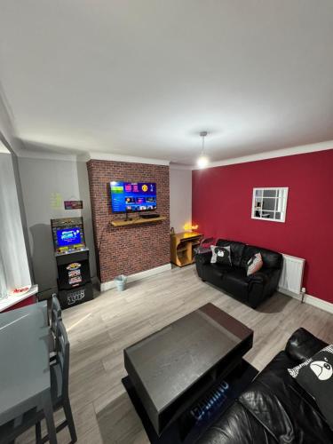 a living room with a black couch and a red wall at Giga Residential 4 Bedrooms, 8 guests , Near City Centre, Arcade Machine, Sky TV, Netflix, Free Wifi, Free Parking in Newcastle upon Tyne