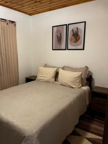 a bedroom with a bed with two pictures on the wall at Casa Recanto 3 in Campos do Jordão