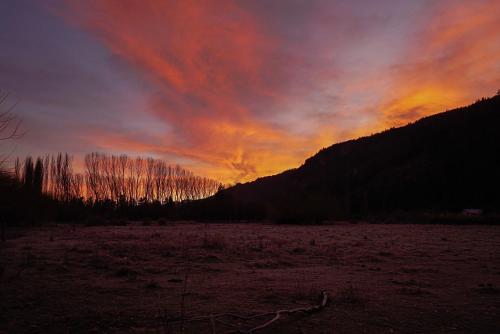una puesta de sol en un campo con árboles en el fondo en Cabañas Patagonia Rupestre en El Bolsón