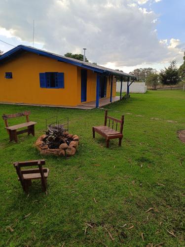 a building with benches and a fire pit in a field at Casa Amarela in Lages