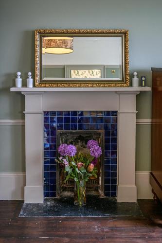 a fireplace with a mirror and flowers in a vase at House of the Northern Gate - a luxury baronial house that sleeps 18 guests in 9 bedrooms in Thurso