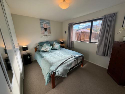 een slaapkamer met een bed met een blauw dekbed en een raam bij 11 Dorset Street in Hanmer Springs