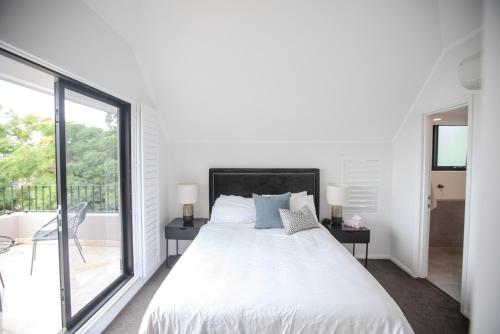 a white bedroom with a bed and a balcony at PHOE1-3B - Harbour Haven Townhouse in Sydney