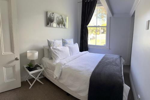 um quarto com uma cama com lençóis brancos e uma janela em SHORT WALK TO NELSON CITY CENTRE - Quiet location, comfy beds, pet friendly, full kitchen, claw-foot bath tub, outdoor areas em Nelson