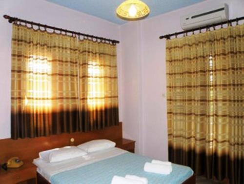 a bedroom with a bed and two windows with curtains at Hotel Kavouris in Skopelos Town