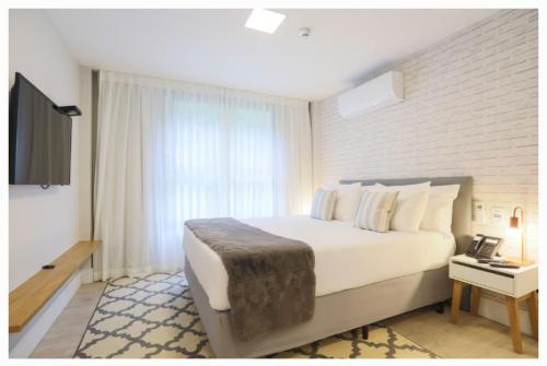 um quarto com uma grande cama branca e uma janela em Carpe Diem Boutique - Apart com banheira em Campos do Jordão