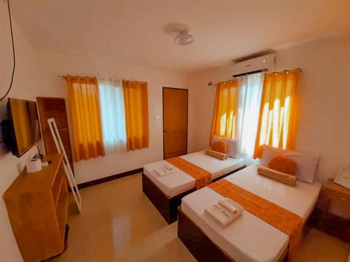 two beds in a room with orange curtains at MKB Pension in Coron