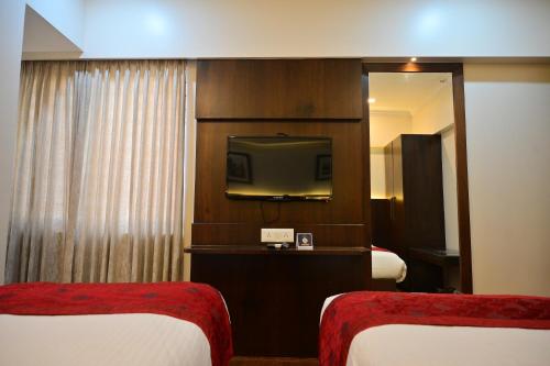 um quarto de hotel com duas camas e uma televisão em Hotel Golden Riviera em Mysore