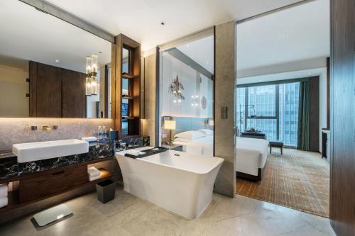 a bathroom with a large white tub and a bedroom at Sheraton Kunming in Kunming