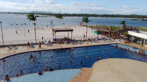 people in a swimming pool next to a beach at Golden Lake Apart Hotel Arraial do Cabo RJ A&J 2 in Arraial do Cabo