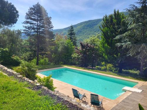 una piscina con 2 sillas y una montaña en Lou mas del ranc, en Roquestéron