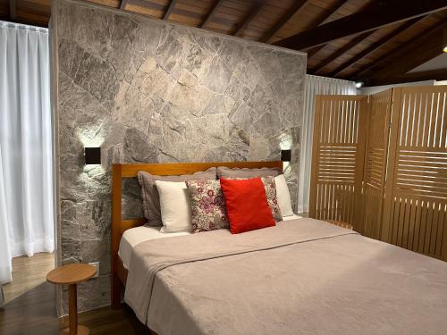 een slaapkamer met een bed met een stenen muur bij Chalé Requinte da Serra in Miguel Pereira