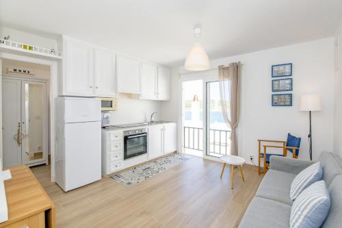 a kitchen and living room with white cabinets and a couch at Ponent-Apartamento frente al mar, refugio costero in Es Grau