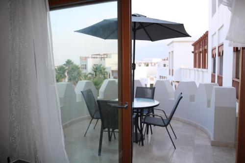 einen Balkon mit einem Tisch, Stühlen und einem Sonnenschirm in der Unterkunft Jabal Sifah Tha Marina View Apartment in Muscat