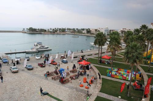 a group of people standing around a park with a boat in the water at Jabal Sifah Tha Marina View Apartment in Muscat