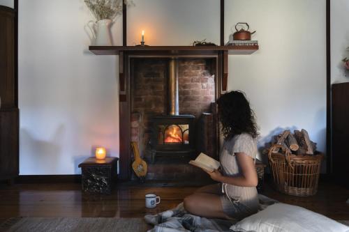 a woman sitting on the floor reading a book in front of a fireplace at Pickers Hut in Basket Range