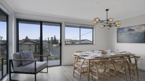 a dining room with a table and chairs and windows at 'Clear Water at The Entrance' by HolidayCo in The Entrance