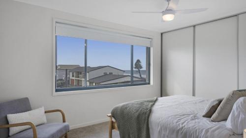 a bedroom with a large window and a bed and a chair at 'Clear Water at The Entrance' by HolidayCo in The Entrance