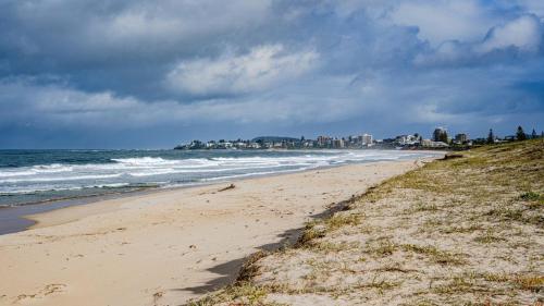 a beach with the ocean and buildings in the background at 'Clear Water at The Entrance' by HolidayCo in The Entrance