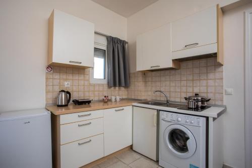 a kitchen with white cabinets and a washing machine at Economisa Apartments in Ialyssos