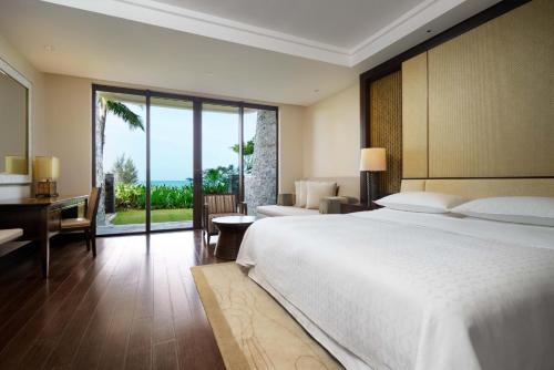 Sheraton Shenzhou Peninsula Resort في اننينغ: غرفة نوم بسرير كبير ومكتب ونافذة