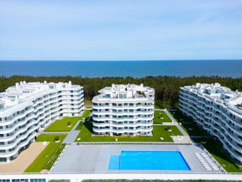 three apartment buildings with a swimming pool in front of the ocean at Rogowo Pearl City Apartments in Rogowo