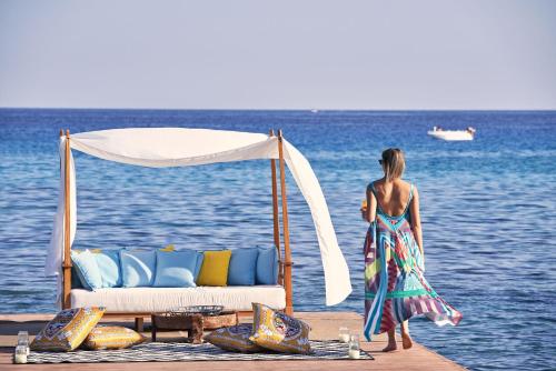 una mujer parada en un muelle cerca del agua con una cama en Aquagrand Exclusive Deluxe Resort Lindos - Adults only, en Lindos