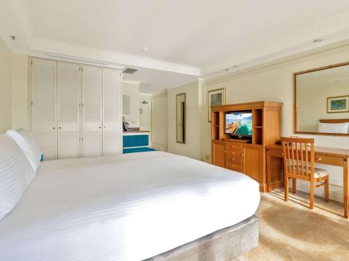 a bedroom with a bed and a desk and a television at Pullman Cairns International in Cairns