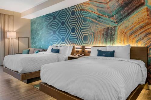 two beds in a hotel room with a mural at Cambria Hotel St Petersburg-Madeira Beach Marina in St. Pete Beach