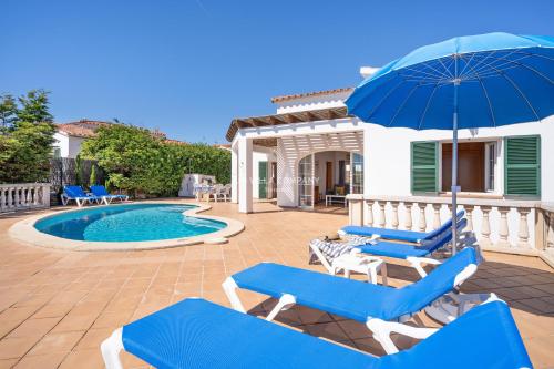 a patio with blue chairs and an umbrella and a pool at Villa CASSIA in Cala en Porter