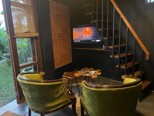 a room with two chairs and a table and a tv at KUBU BLACK HOUSE in Jembrana