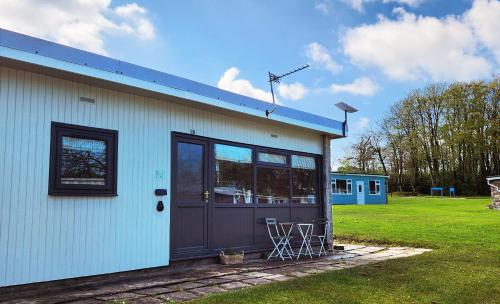 a white building with a door and a lawn at 18 Bucklands - Cosy 5-Star Chalet - Starlink Wi-Fi - Coastal Woodland in Bucks Mills