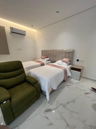 1 dormitorio con 2 camas y silla verde en سرايا الخليجية, en Al Hofuf