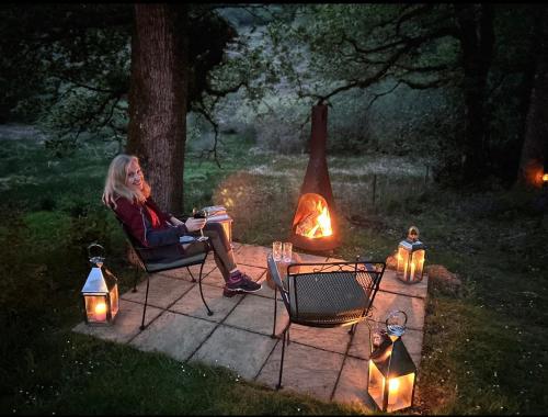 a woman sitting in a chair next to a fire at Strathlachlan Lodge, Luxury Country House with Hot tub & Sauna in Strachur