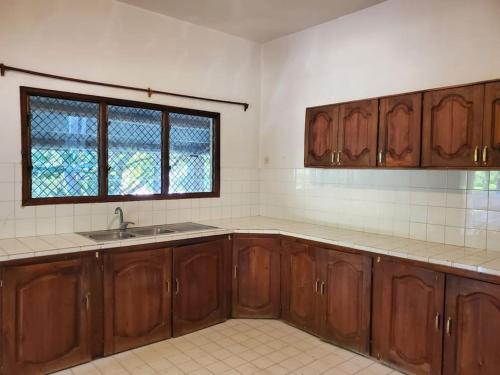 Una cocina con armarios de madera y un fregadero y una ventana. en Charmante villa familiale proche de la mer, en Mahajanga