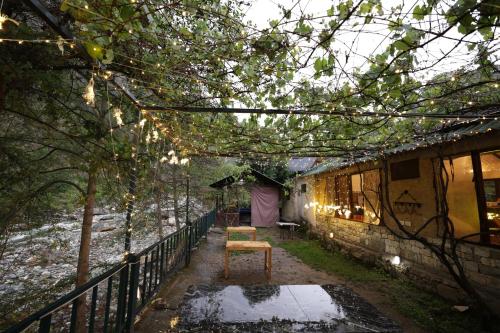 a patio with a chair and a fence with lights at Thehraav By The River - Mudhouse Odyssey, Tirthan Valley in Banjār