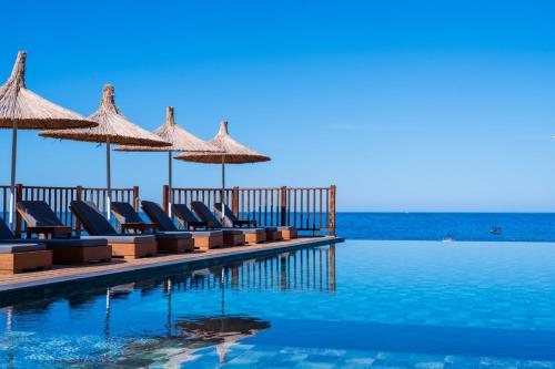 a pool with chairs and umbrellas and the ocean at Sea Valley Lodge in Faralya
