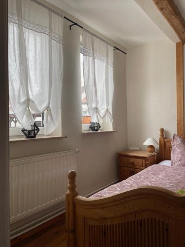 a bedroom with a bed and two windows with white curtains at Ratstraße im Kyffhäuser - krumm & schief in Bad Frankenhausen